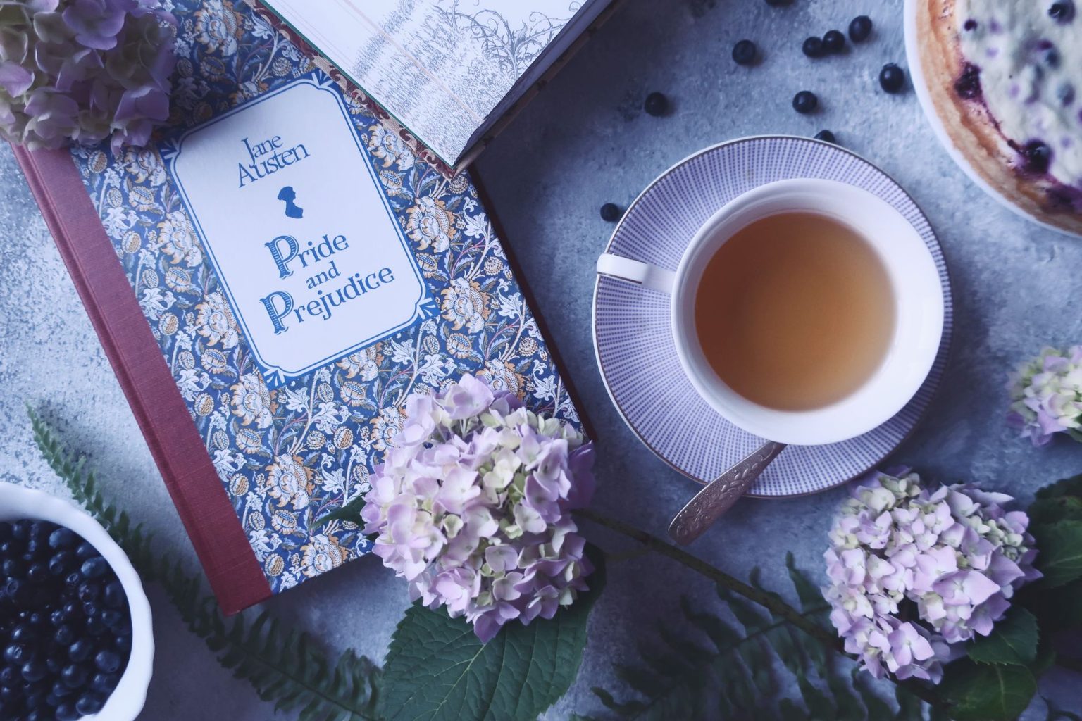 Livro “Orgulho e Preconceito” ao lado de uma xícara de chá e flores sobre uma superfície clara