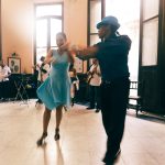 Casal dança em um salão elegante, em uma cena que remete aos musicais clássicos.
