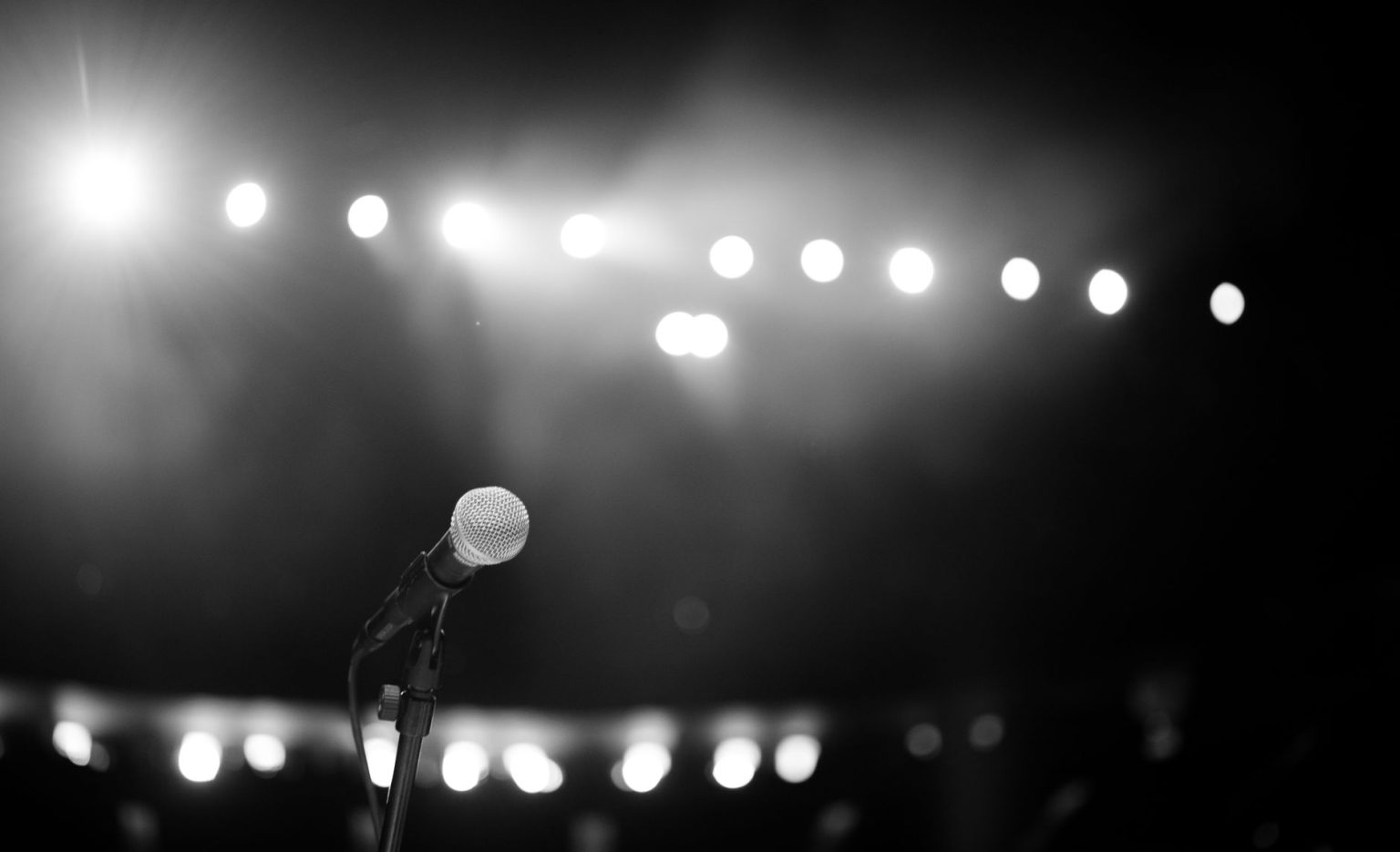 Microfone em um palco iluminado por fortes luzes, em uma imagem em preto e branco.