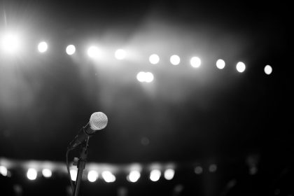 Microfone em um palco iluminado por fortes luzes, em uma imagem em preto e branco.