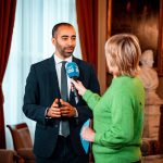 Jornalista entrevista um profissional durante um evento do setor de mídia.