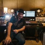 Produtor musical sentado em um estúdio de gravação diante de equipamentos e monitores.