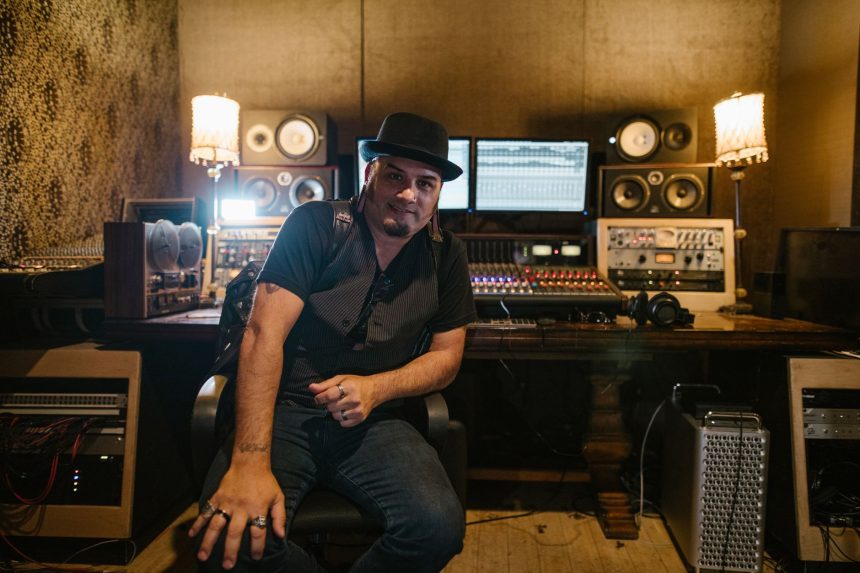 Produtor musical sentado em um estúdio de gravação diante de equipamentos e monitores.