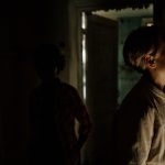 Interior abandonado e pouco iluminado, com figuras indistintas projetando sombras em uma atmosfera sombria e misteriosa.