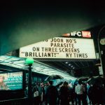 Público se reúne à noite diante de um cinema em Nova York, sob a marquise iluminada.