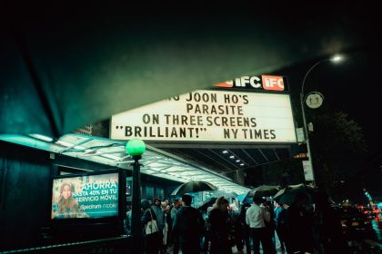 Público se reúne à noite diante de um cinema em Nova York, sob a marquise iluminada.