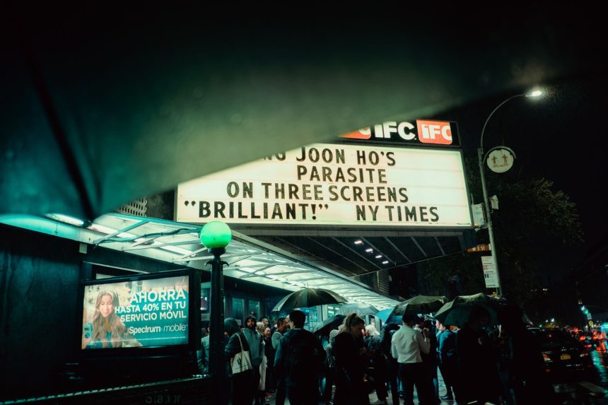 Público se reúne à noite diante de um cinema em Nova York, sob a marquise iluminada.