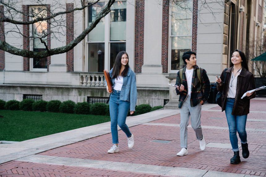 Grupo diverso de estudantes caminhando por uma calçada do campus universitário em um dia ensolarado.