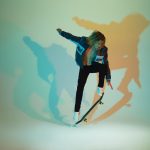 Skateboarder realiza uma manobra em ambiente com iluminação colorida e sombras dinâmicas.