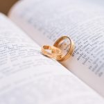 Alianças douradas sobre uma Bíblia aberta, em composição associada a casamento e votos.