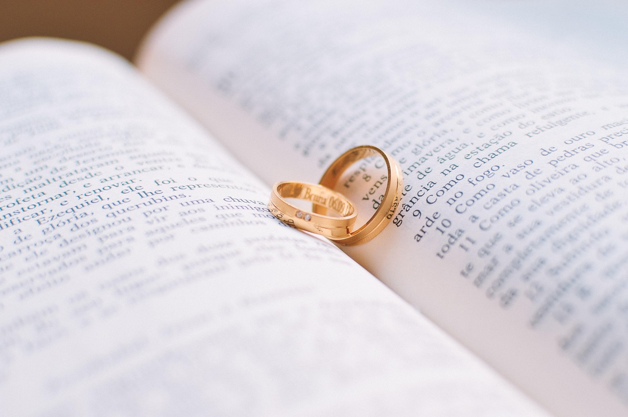 Alianças douradas sobre uma Bíblia aberta, em composição associada a casamento e votos.